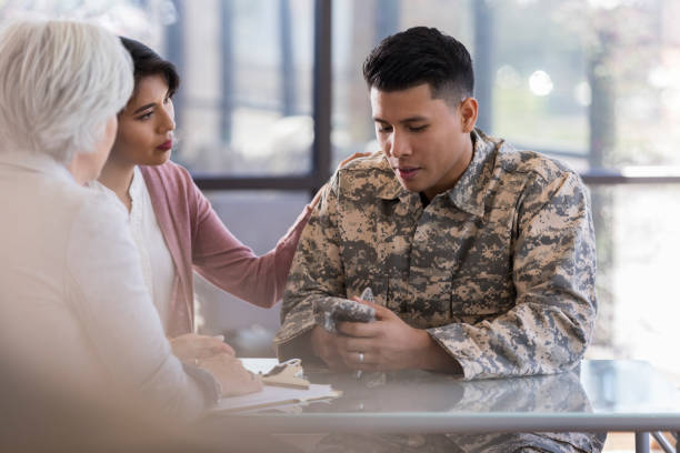 istock Young, military male looks down at his hands while speaking with counselor 1087566182