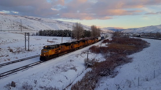 Train passing by Ogden Utah while sun was setting on a cold, snowy, winter day.