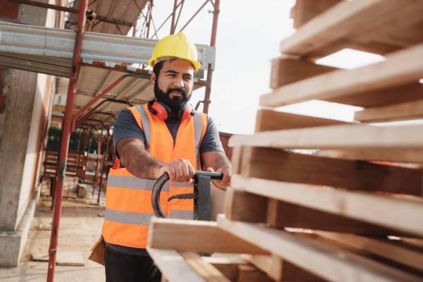 Latino Manual Worker With Forkift Pallet Stacker In Construction Site Skilled people working in construction site. Hispanic man at work in new housing project. Professional latino worker using manual pallet jack to move material. pallet jack handle stock pictures, royalty-free photos & images