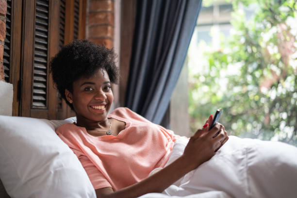 istock Afro Young Woman Using Smartphone While Lying Down in Bed Portrait 1087585010