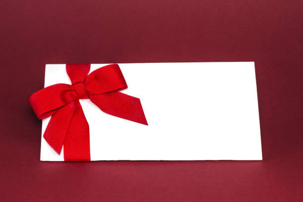 istock Gift isolated white card with red ribbon bow on deep red background. 1087593254