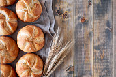 Crusty round bread rolls, known as Kaiser or Vienna rolls scattered on linen towel on rustic wood, flat lay