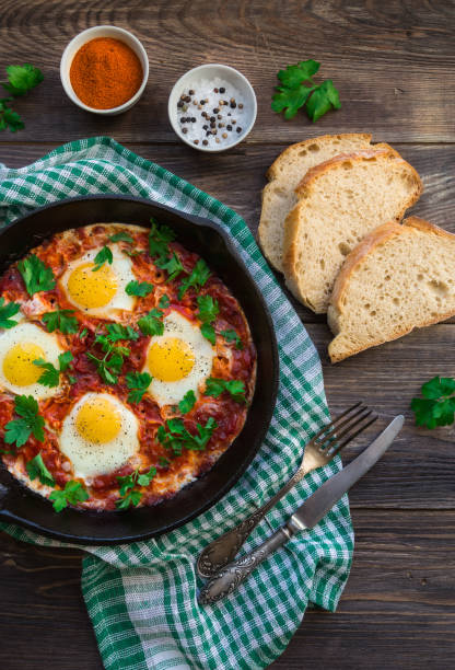 istock Fried eggs with vegetables and tomato sauce in iron skillet on rustic wooden background. 1087602252