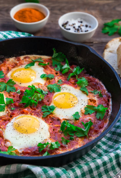 istock Fried eggs with vegetables and tomato sauce in iron skillet on rustic wooden background. 1087602340