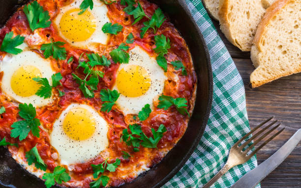 istock Fried eggs with vegetables and tomato sauce in iron skillet on rustic wooden background. 1087602352