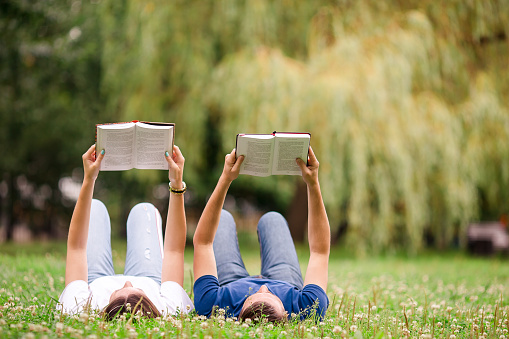 Young romantic couple lying in park and reading books