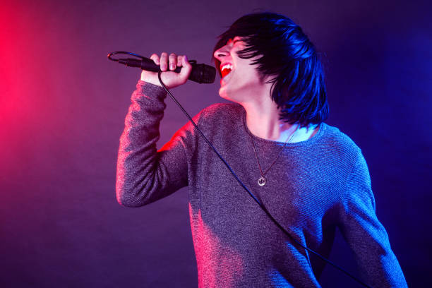 screaming vocalist on concert The young guy vocalist is screaming in microphone on stage on concert illuminated with red and blue lights. emo boy stock pictures, royalty-free photos & images