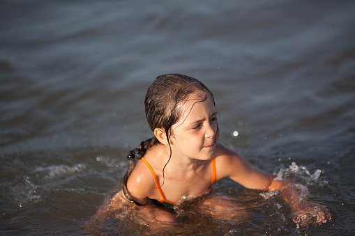 Happy little girl whit water wings swims swimming in river during summer day