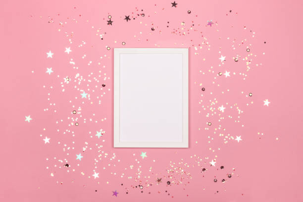 istock Festive background with blank white photo frame on pink with confetti. 1087648886