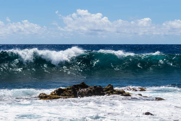 istock Wave breaking offshore in Hawaii; volcanic rock and foam in foreground. Blue ocean, sky, clouds in background. 1087657934
