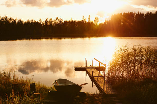 Summer sunset on the shore of a Finnish lake, with a small pier and a boat.