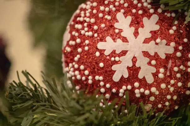 Red sparkly ornament/sphere with a white snowflake cut-out and small white dot "snowflakes" in a Christmas tree.