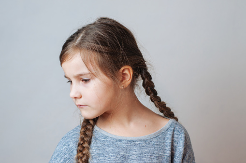 Sad little girl with pigtails portrait on a neutral grey background