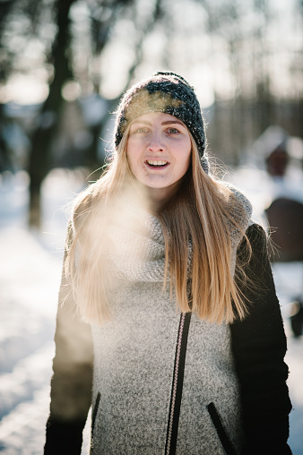 Portrait of a happy young girl jumping and enjoying snow in a winter park.