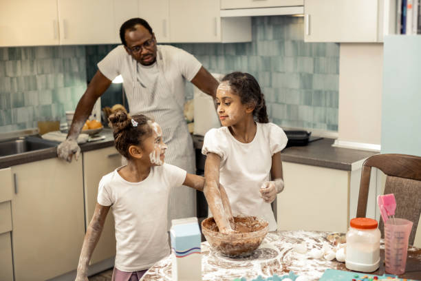 istock Father wearing striped apron watching his girls making cupcakes 1087722012