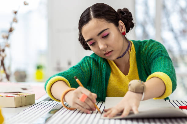 istock Young dark-haired asian dressmaker with pink eyeshadows preparing a pattern 1087729042
