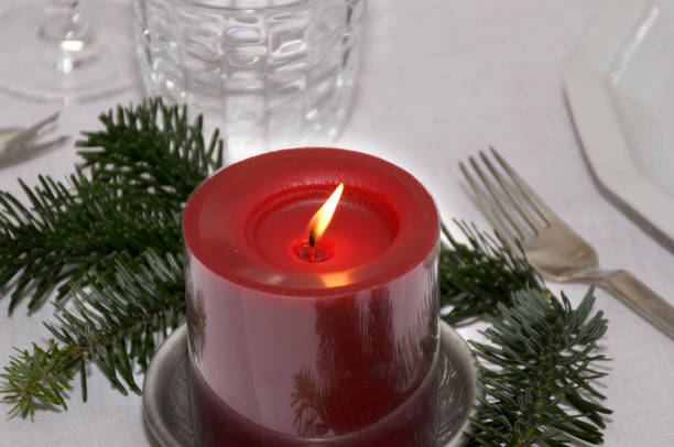 Colorful red Christmas candle with pine foliage burning on a festive table set with cutlery and glassware