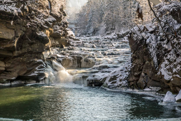 icy winter waterfall steaming between stones, orange sunlight, frozen pond