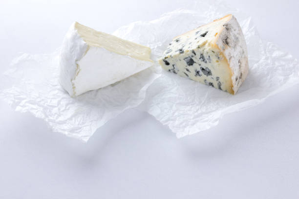 camembert und blauschimmelkäse auf pergamentpapier. stücke von verschiedenen käse auf weißem hintergrund. dorblu und weichkäse im stil des minimalismus. öko-milchprodukte - weichkäse stock-fotos und bilder