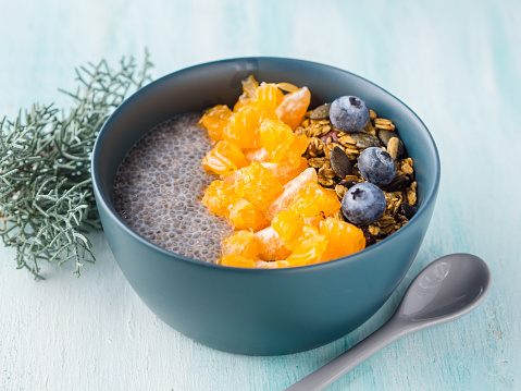 Chia pudding with tangerines and matcha tea granola in a bowl on pastel turquoise wooden background. Plant based breakfast