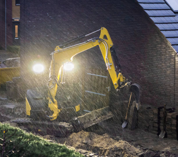 ground worker working at night in bad rainy weather, constructing a garden in the evening