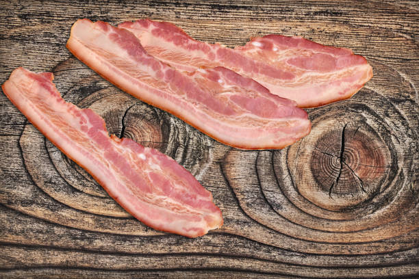 istock Three Pork Bacon Rashers Set On Old Knotted Weathered Cracked Pinewood Picnic Table Rustic Rough Grunge Surface 1087803670