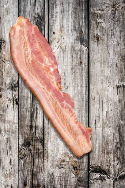 istock Single Pork Bacon Rasher On Old Knotted Weathered Cracked Pinewood Picnic Table Rustic Rough Grunge Surface 1087803912