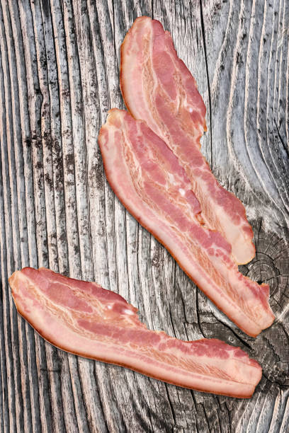 istock Three Pork Bacon Rashers Set On Old Knotted Weathered Cracked Pinewood Picnic Table Rustic Rough Grunge Surface 1087803914