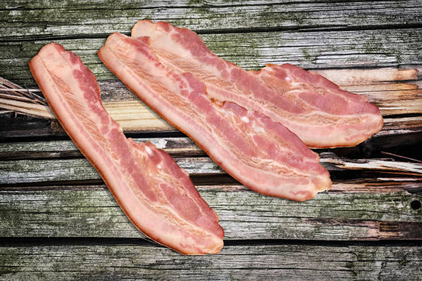 istock Three Pork Bacon Rashers Set On Old Knotted Weathered Cracked Pinewood Picnic Table Rustic Rough Grunge Surface 1087805264