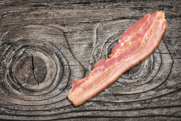 istock Single Pork Bacon Rasher On Old Knotted Weathered Cracked Pinewood Picnic Table Rustic Rough Grunge Surface 1087806300