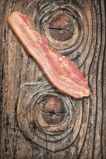 istock Single Pork Bacon Rasher On Old Knotted Weathered Cracked Pinewood Picnic Table Rustic Rough Grunge Surface 1087806582