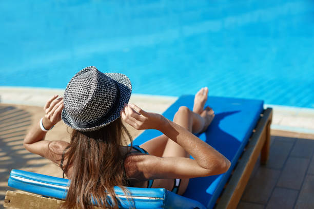 Woman in hat lying on a lounger near the swimming pool with space for your text Woman in hat lying on a lounger near the swimming pool with space for your text. chaise longue woman stock pictures, royalty-free photos & images