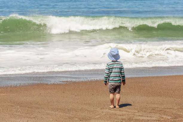Small kid standing on the beach enjoying beautiful waves of the Pacific Ocean