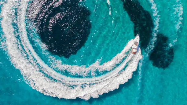 Drone view above yacht cruising through flat calm blue Mediterranean water.