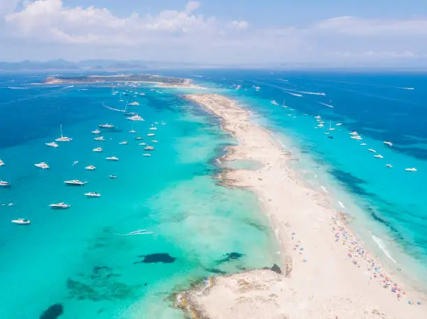 Aerial overhead view of large amount of yachts anchored off the coast of Formentera Ibiza, with turquoise Mediterranean Sea and ocean blue water.