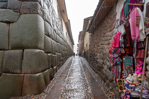 Cusco, Peru - Oct 14, 2018: A narrow street in central Cusco with old colonial architecture, cobblestone roads, and some people walking.