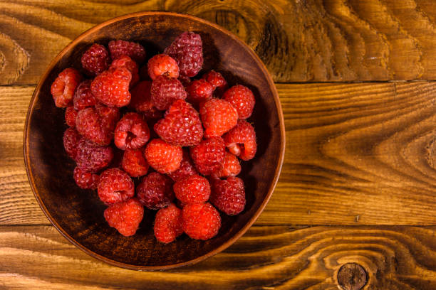 istock Ceramic plate with ripe raspberries on wooden table. Top view 1087875690