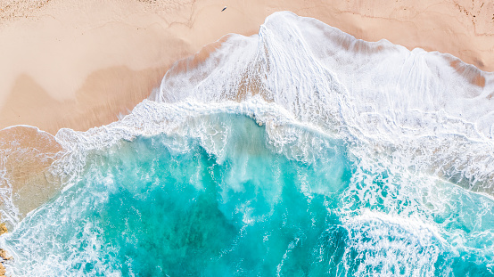 Aerial drone overhead view of huge beach and dynamic sandy, rocky coastline with large crashing foamy waves over turquoise water.