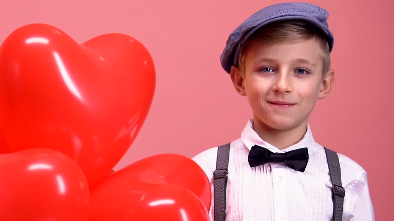 Shy little boy with heart-shaped balloons smiling to camera, Valentines day gift