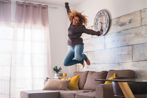 crazy middle age woman jump at home over the sofa to celebrate success - joyful and happiness people concept - craziness and freedom lifestyle for independent modern female