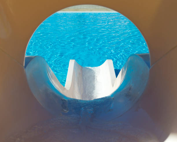 This is a shot showing the view to the bottom of a short water slide.  The water at the bottom is a very vibrant blue while the surrounding plastic slide is tan.  Focus is on the bottom of the slide.