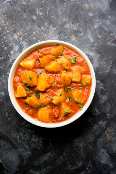 Indian food - Aloo curry masala. Potato cooked with spices and herbs in a tomato curry. served in a bowl over moody background. selective focus stock photo