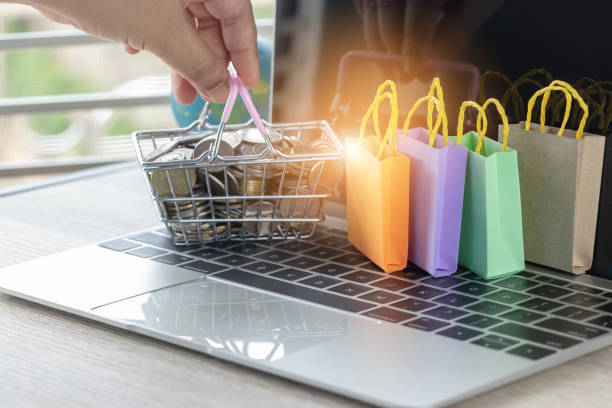 Hand holding basket of Thai coins and shopping bags on laptop keyboard with globe nearby. Consumer can buy products directly anywhere from seller over internet. Online shopping and e-commerce concept. mano que sostiene la canasta de monedas tailandesas y bolsas en el teclado del ordenador portátil con globo de cerca. consumidores pueden comprar productos directamente en cualquier vendedor en internet. concepto de compras y de comercio electrónico en l