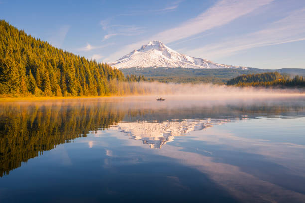 Senior man fishing on a canoe in Trillium Lake at Sunrise with views of Mount Hood An active senior man fishing on a canoe at Trillium Lake in Oregon at the water's edge of the lake to see Mount Hood peak during sunrise. Fisherman at trillium lake going fishing. Early morning fishing for trout on a canoe or kayak. Golden hour Mount Hood lake Trillium canoe. Mount Hood had golden light shining on the peak at sunrise. A beautiful sunrise at Trillium lake near Portland, Oregon in the Pacific Northwest. Reflections of Mt Hood were seen in Trillium Lake. There were amazing clouds during sunset at Trillium lake with a view of Mount Hood. mt hood stock pictures, royalty-free photos & images
