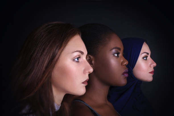 Maquillaje. Retrato de tres mujeres. Mujeres caucásicas y afroamericanas posando en estudio sobre fondo negro. - foto de stock