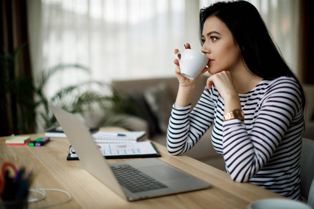 istock Young thoughtful woman having coffee while working on laptop at home 1088104624