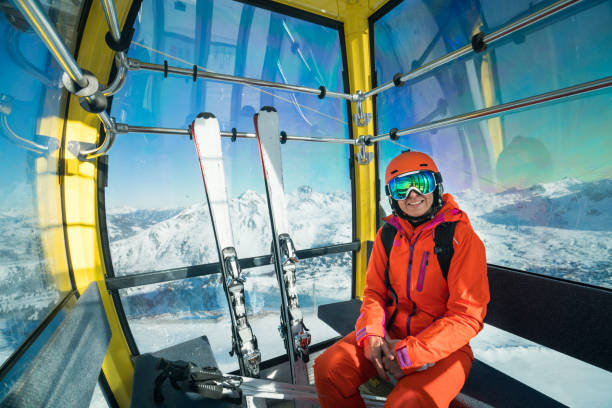 smiling skiing woman going up with cable car in winter mountains happy smiling female skier with skiing googles and helmet sitting in cable car up to austrian mountains on sunny winter day overhead cable car stock pictures, royalty-free photos & images