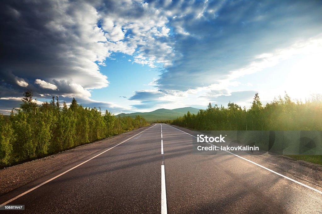 A long road with trees on either side and a beautiful sky road in Russian mountains Asphalt Stock Photo