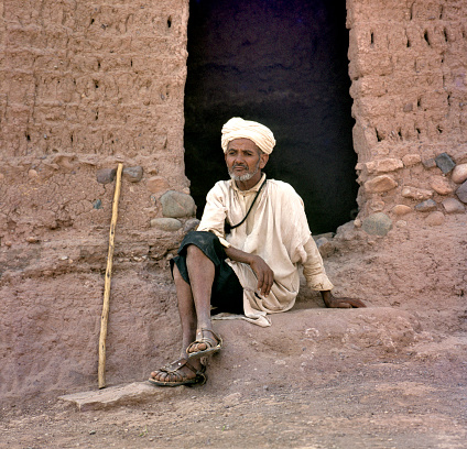 Ksar Ait Benhaddou, Morocco-August 12, 2017: Man resting outside entrance of a small house in the village. This is an old Berber adobe-brick village or kasbah.