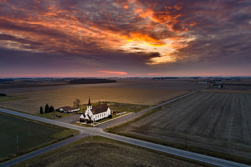 A bright sunset over a little church at a corner road in the country captured via drone in the air.